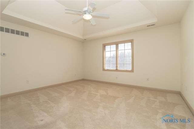 unfurnished room featuring a tray ceiling, visible vents, and light carpet