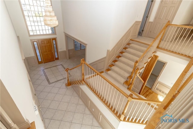 tiled entryway with a high ceiling, wainscoting, a decorative wall, a chandelier, and stairs