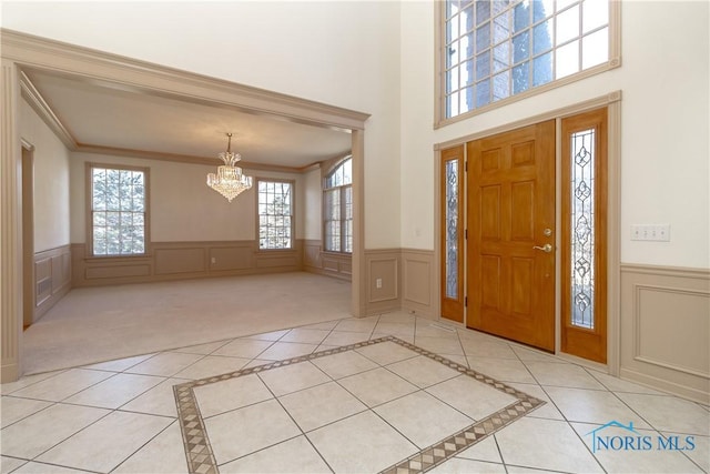 foyer entrance featuring light tile patterned floors, a notable chandelier, wainscoting, and ornamental molding