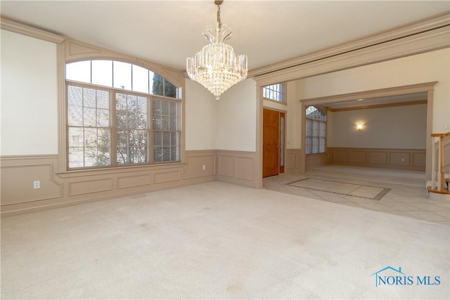 empty room featuring a wainscoted wall, carpet floors, a chandelier, and a decorative wall