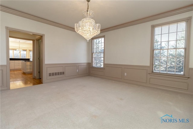 carpeted empty room with a wainscoted wall, crown molding, a notable chandelier, and visible vents