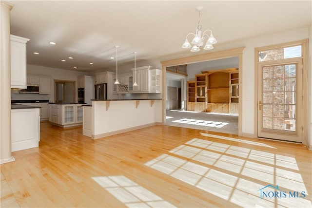 kitchen with light wood-type flooring, pendant lighting, a breakfast bar, dark countertops, and freestanding refrigerator