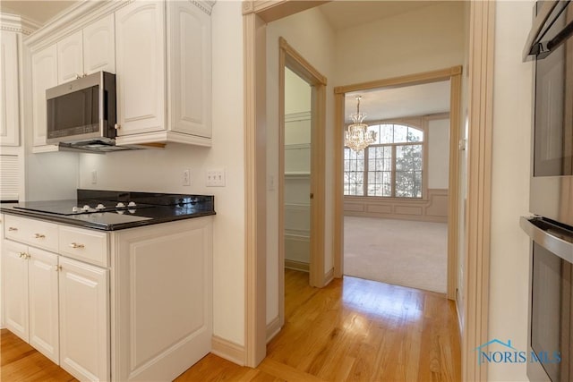 kitchen with light wood-style flooring, stainless steel appliances, white cabinetry, dark countertops, and a notable chandelier