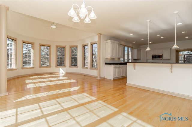 kitchen featuring dark countertops, a breakfast bar, an inviting chandelier, light wood-style floors, and stainless steel microwave