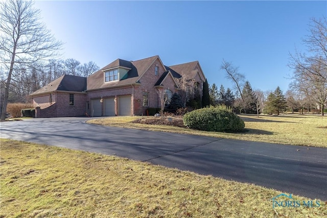 view of front of property with aphalt driveway, an attached garage, a front yard, and brick siding