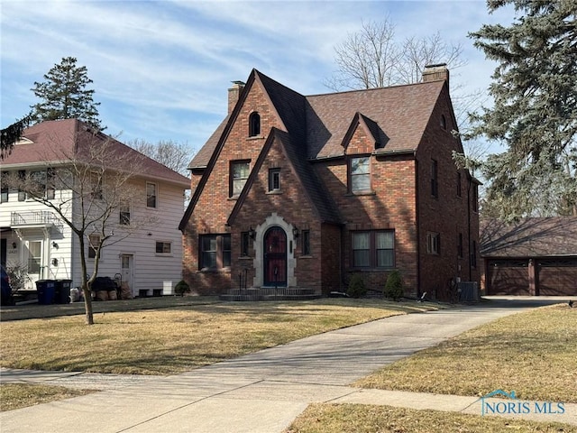 view of front of home with brick siding, a front lawn, roof with shingles, central AC unit, and a chimney