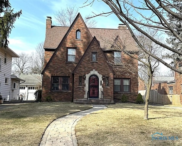 tudor home featuring a front yard, a chimney, and fence