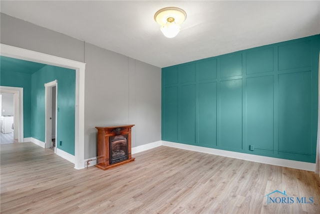 unfurnished living room with a decorative wall, a fireplace, baseboards, and wood finished floors