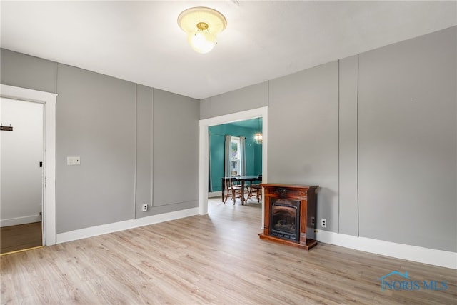 spare room featuring a fireplace, baseboards, and light wood-type flooring