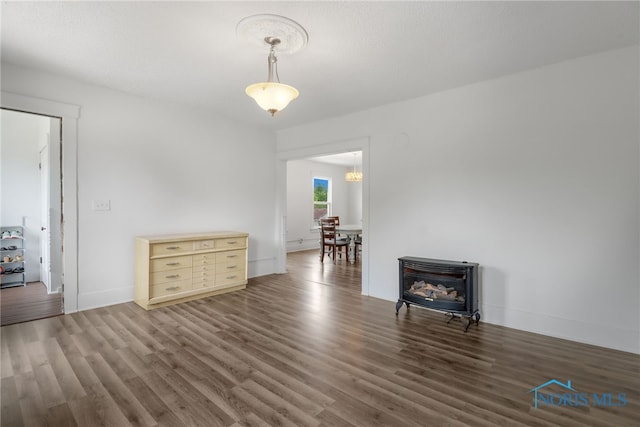 unfurnished dining area with baseboards, an inviting chandelier, wood finished floors, and a wood stove