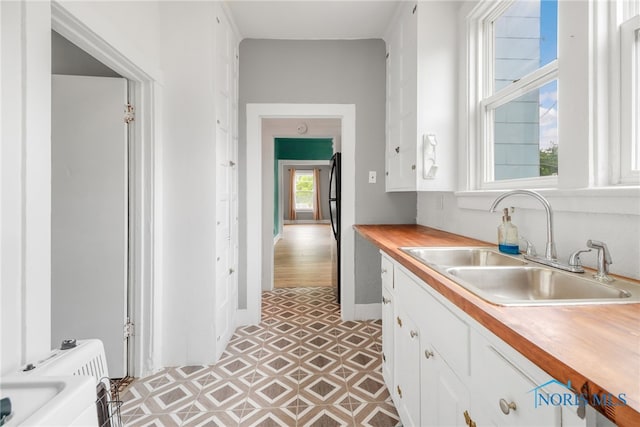 kitchen featuring white cabinetry, baseboards, freestanding refrigerator, and a sink