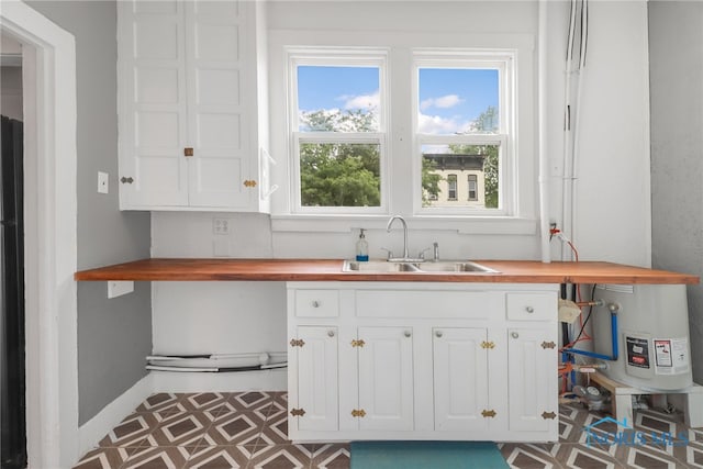 kitchen with tile patterned floors, wooden counters, white cabinetry, and a sink