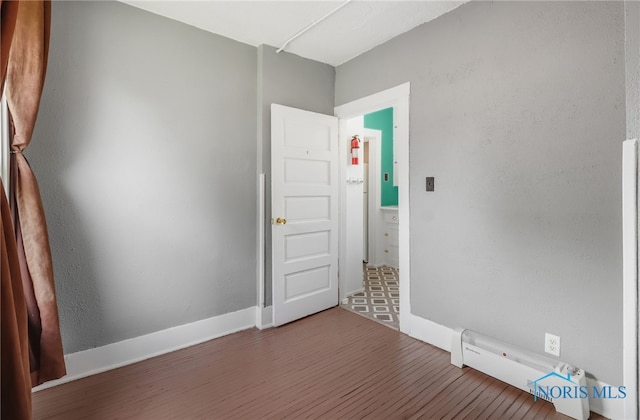 unfurnished room featuring a baseboard heating unit, wood finished floors, and baseboards