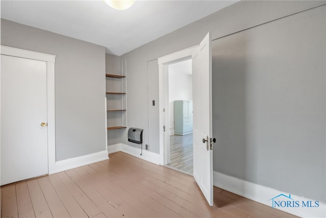 unfurnished room featuring heating unit, baseboards, and wood finished floors