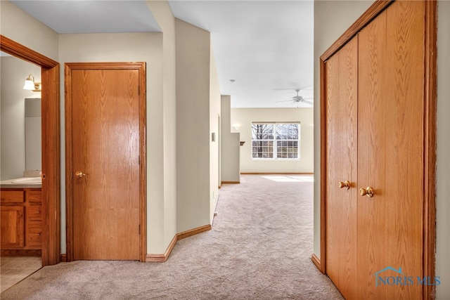 hallway featuring a sink, baseboards, and light carpet