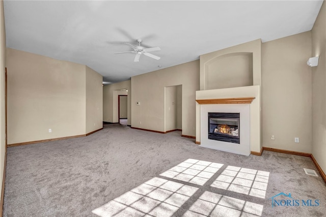 unfurnished living room featuring a glass covered fireplace, visible vents, carpet, and ceiling fan