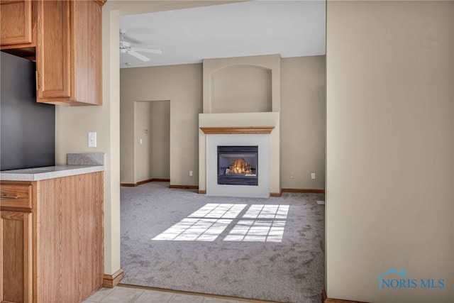 unfurnished living room with light carpet, a glass covered fireplace, baseboards, and a ceiling fan