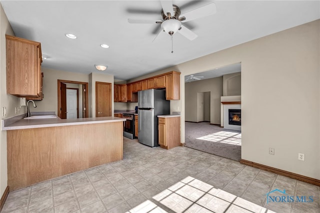 kitchen with a ceiling fan, a peninsula, a sink, stainless steel appliances, and light countertops