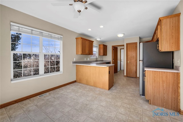 kitchen with a sink, a peninsula, light countertops, baseboards, and ceiling fan