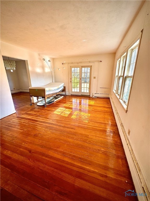 interior space featuring baseboard heating, french doors, a textured ceiling, and wood finished floors