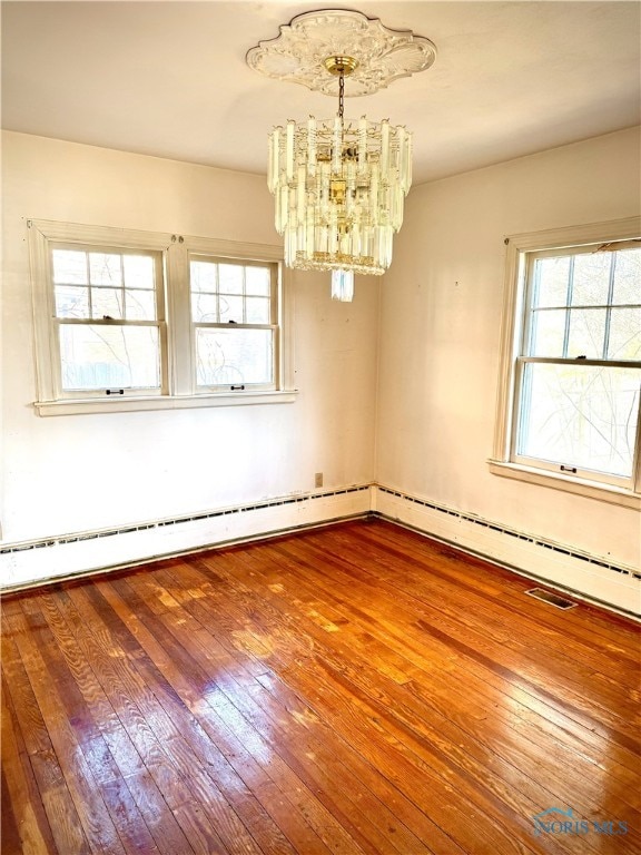 spare room with a chandelier, plenty of natural light, and hardwood / wood-style flooring