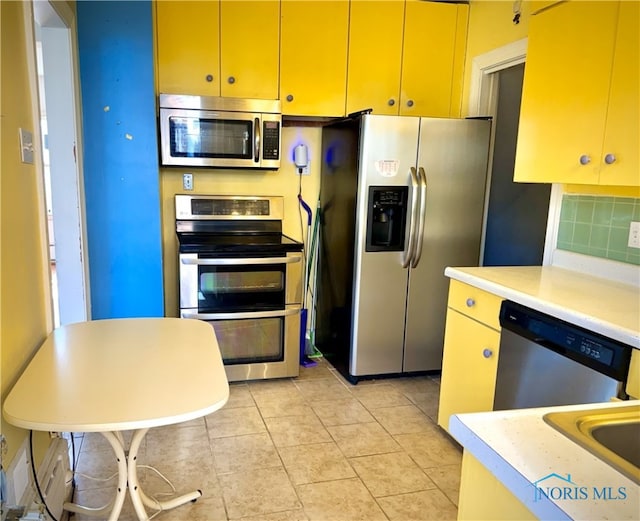 kitchen with tasteful backsplash, appliances with stainless steel finishes, light tile patterned flooring, light countertops, and yellow cabinetry