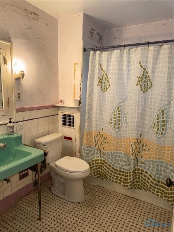 bathroom featuring a wainscoted wall, tile patterned flooring, curtained shower, tile walls, and toilet