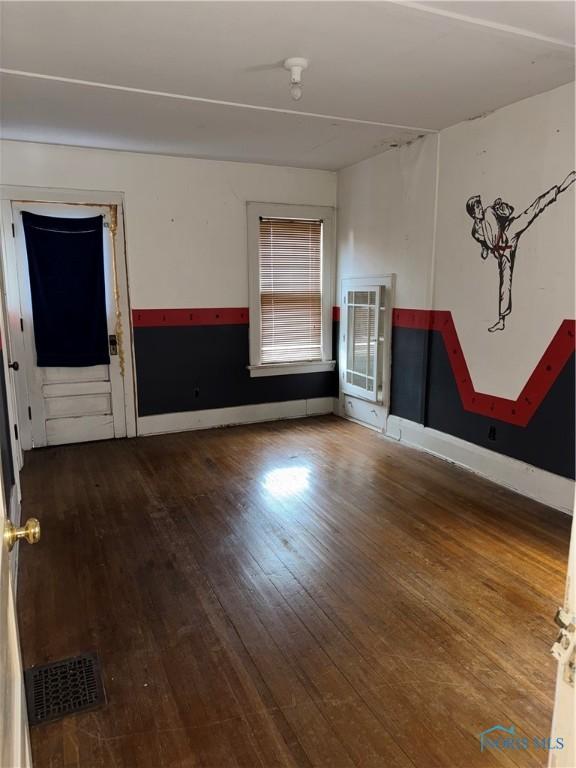 empty room with hardwood / wood-style floors, baseboards, and visible vents