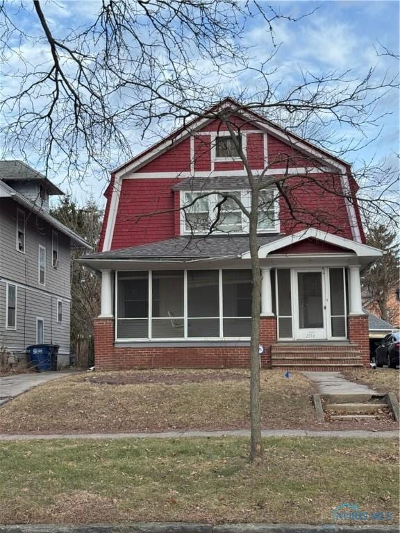 view of front facade featuring entry steps, brick siding, a gambrel roof, and a sunroom