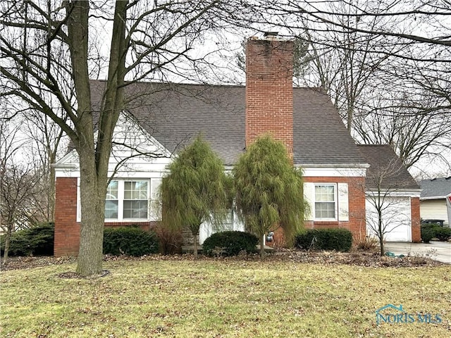 view of front of house with a front yard, an attached garage, driveway, and a shingled roof