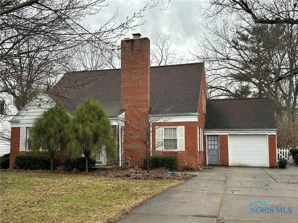 view of front of house with brick siding, concrete driveway, a front yard, a chimney, and an attached garage