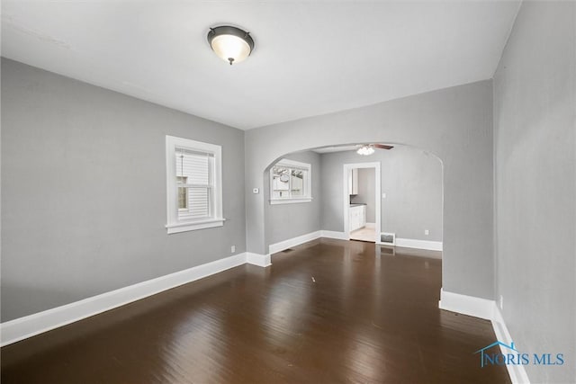spare room with baseboards, wood finished floors, arched walkways, and a ceiling fan