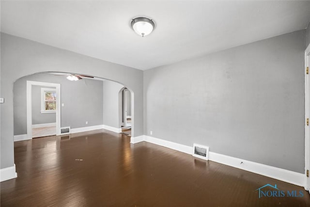spare room featuring a ceiling fan, wood finished floors, baseboards, visible vents, and arched walkways