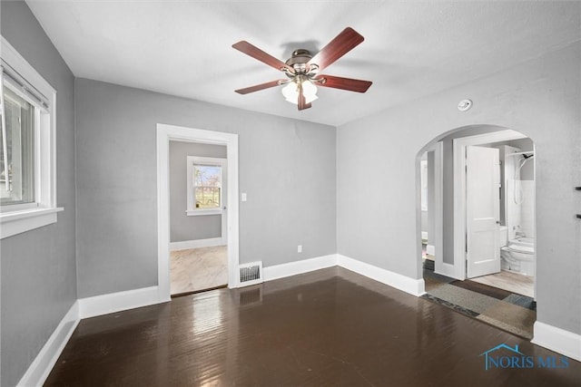 spare room with a ceiling fan, wood finished floors, baseboards, visible vents, and arched walkways