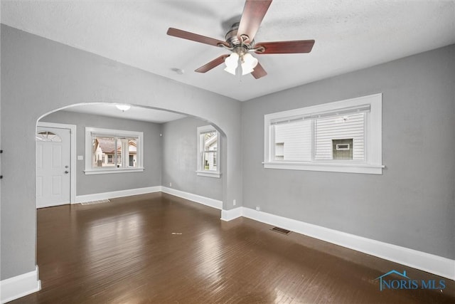 unfurnished room featuring arched walkways, visible vents, a ceiling fan, and wood finished floors