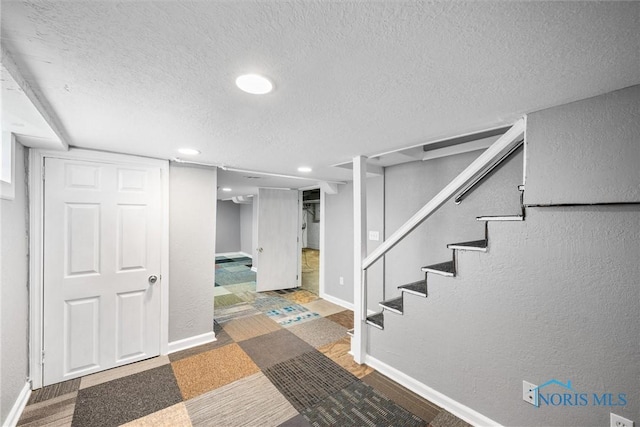finished below grade area featuring baseboards, a textured wall, stairway, and a textured ceiling
