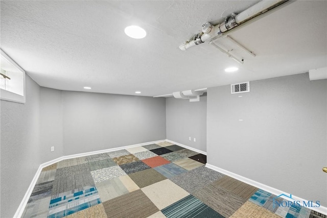finished basement featuring baseboards, a textured ceiling, visible vents, and recessed lighting
