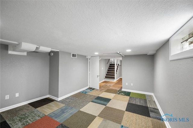basement featuring baseboards, a textured ceiling, visible vents, and stairway