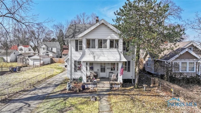 view of front facade with a front yard, fence, covered porch, and a chimney