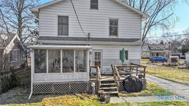 rear view of house featuring a deck, fence, a shingled roof, and a sunroom