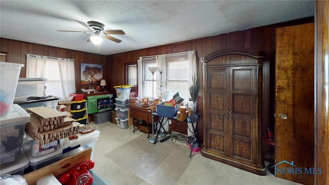 carpeted office featuring plenty of natural light, a ceiling fan, wood walls, and a textured ceiling