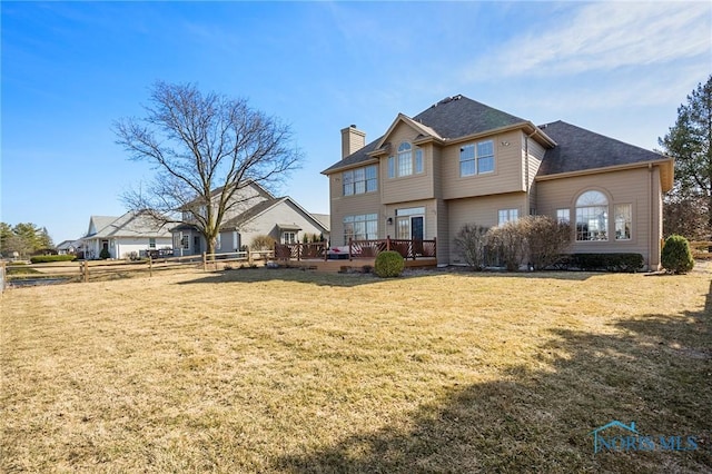 back of property featuring a deck, a lawn, a shingled roof, and a chimney