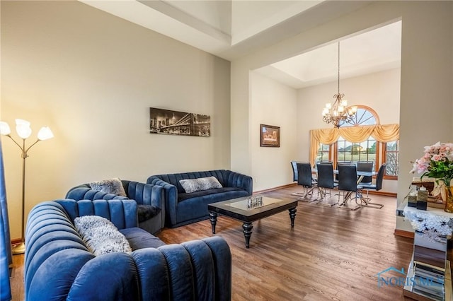 living area with a tray ceiling, wood finished floors, a high ceiling, baseboards, and a chandelier