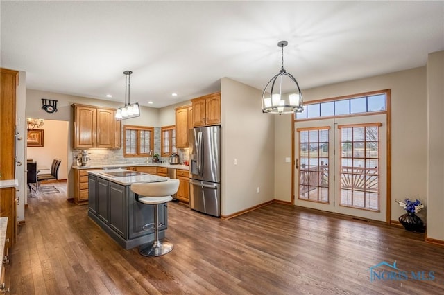 kitchen with light countertops, dark wood-type flooring, stainless steel refrigerator with ice dispenser, backsplash, and a center island