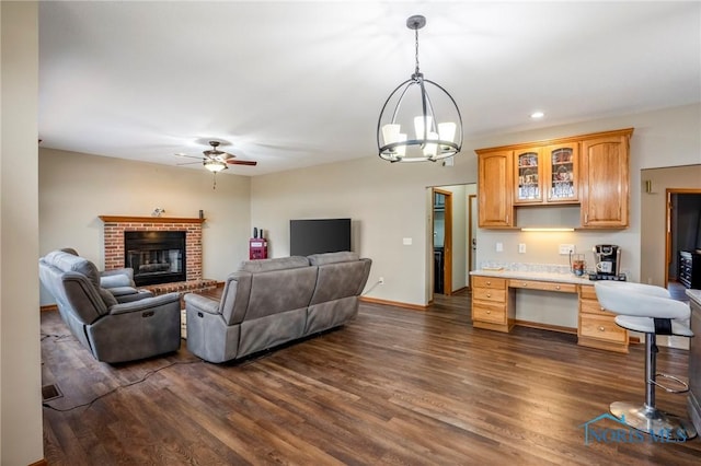 living area featuring a brick fireplace, baseboards, recessed lighting, ceiling fan with notable chandelier, and dark wood-style floors