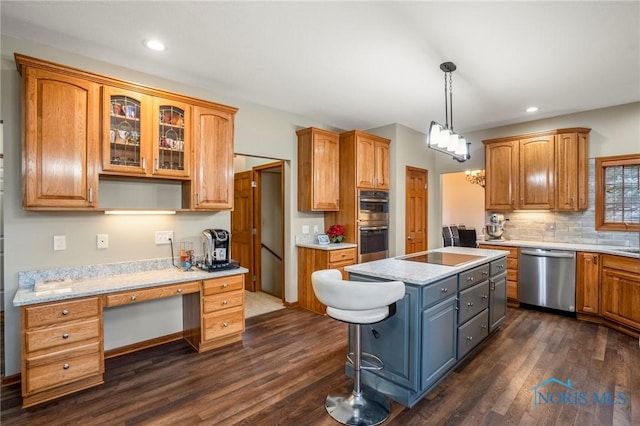 kitchen featuring dark wood-style flooring, decorative backsplash, built in desk, appliances with stainless steel finishes, and a center island