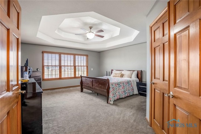 carpeted bedroom with baseboards, a raised ceiling, and a ceiling fan