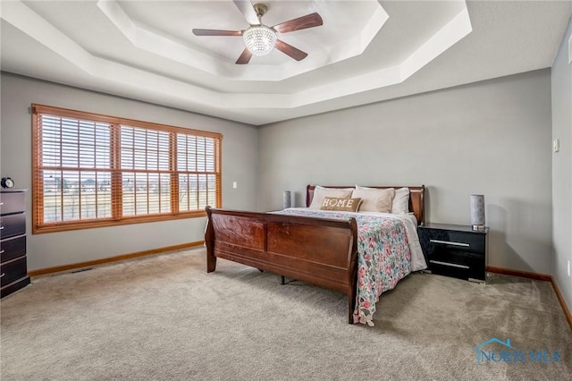 carpeted bedroom featuring a tray ceiling, baseboards, visible vents, and ceiling fan