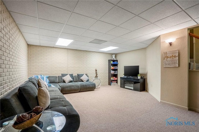 carpeted living room with a drop ceiling, baseboards, and brick wall