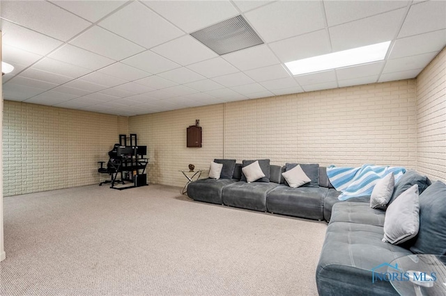 carpeted living room with a paneled ceiling, visible vents, and brick wall